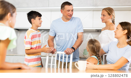Friendly family gathered at table and cheerfully discuss past day. Friendly family gathered at table and cheerfully discuss past day. 128802478