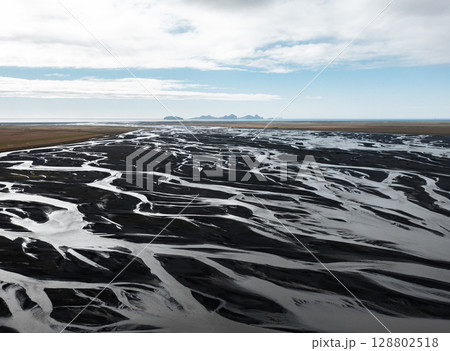 Aerial view of glacial river delta in Iceland Vestmannaeyjar with black sand patterns flowing into the ocean. Concept of raw earth, climate forces, water systems, natural design and Arctic minimalism. Aerial view of glacial river delta in Iceland Vestmannaeyjar with black sand patterns flowing into the ocean. Concept of raw earth, climate forces, water systems, natural design and Arctic minimalism. 128802518