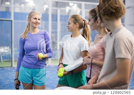 Teenage boy, girl and adult women standing in padel court and talking 128802565