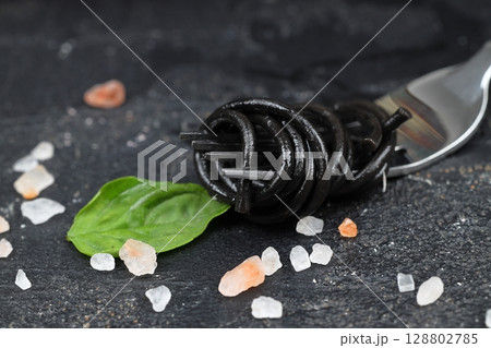 black pasta with cuttlefish ink and green basil leaves on a black fork. Pasta of durum wheat semolina with squid ink. 128802785