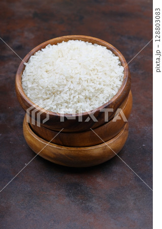 Raw white rice on black background. Long uncooked rice in wooden plate. Natural organic food. Traditional Asian cereal culture. 128803083