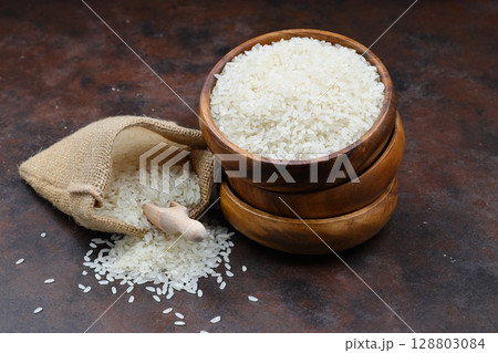 Raw white rice on black background. Long uncooked rice in wooden plate. Natural organic food. Traditional Asian cereal culture. 128803084