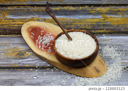 Raw white rice on black background. Long uncooked rice in wooden plate. Natural organic food. Traditional Asian cereal culture. 128803123