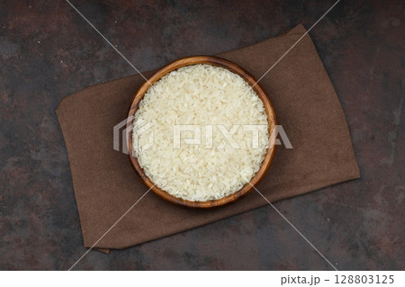 Raw white rice on black background. Long uncooked rice in wooden plate. Natural organic food. Traditional Asian cereal culture. 128803125