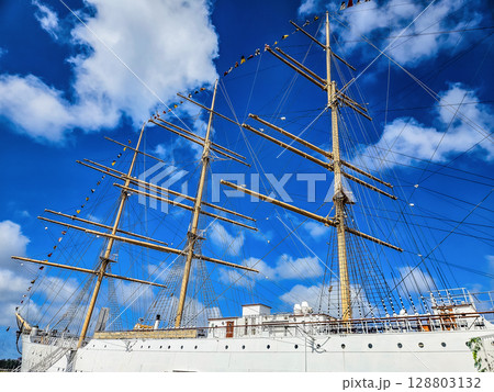 Sailing ship with tall masts and flags under bright blue sky with clouds. High quality photo Sailing ship with tall masts and flags under bright blue sky with clouds. High quality photo 128803132