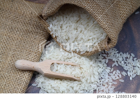 Raw white rice on black background. Long uncooked rice in wooden plate. Natural organic food. Traditional Asian cereal culture. Raw white rice on black background. Long uncooked rice in wooden plate. Natural organic food. Traditional Asian cereal culture. 128803140