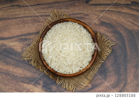 Raw white rice on black background. Long uncooked rice in wooden plate. Natural organic food. Traditional Asian cereal culture. 128803188