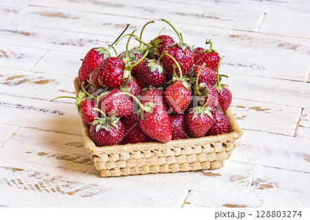 On the wooden surface is a wicker basket with ripe strawberries 128803274