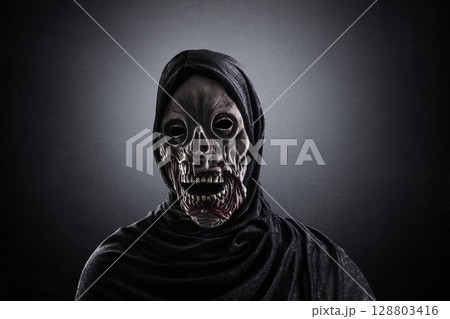 Portrait of a zombie with hooded cape over dark misty background Portrait of a zombie with hooded cape over dark misty background 128803416