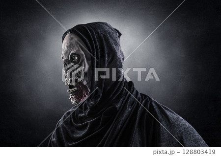 Portrait of a zombie with hooded cape over dark misty background Portrait of a zombie with hooded cape over dark misty background 128803419