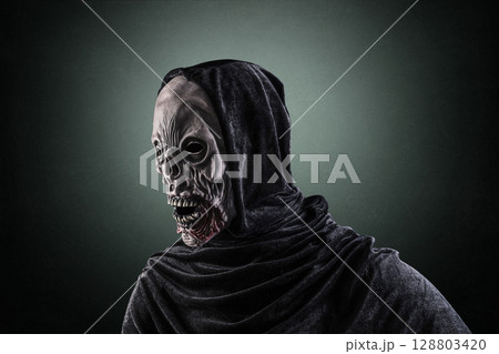Portrait of a zombie with hooded cape over dark green misty background 128803420