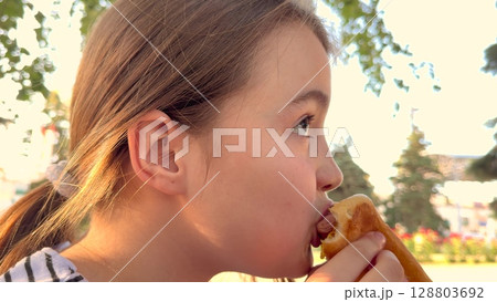 Enjoying summer with a tasty burger, Girl sits in the sunshine, Big bite makes her happy, Her eyes are wide with joy, The park is green and pretty, She loves the fresh air, The burger looks juicy 128803692