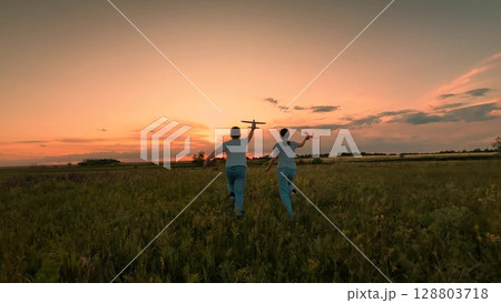 Two kids flying toy planes evening, Joyful moments nature sunset, Friends chasing dreams sun sets, Summer evening fun with toy airplanes, Carefree kids running through meadow dusk, Friendship and 128803718