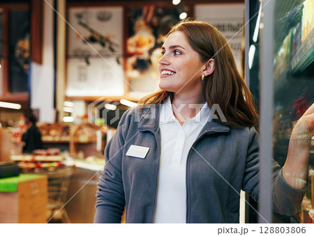 Young smiling female grocery store worker standing at the fridge and looking away 128803806