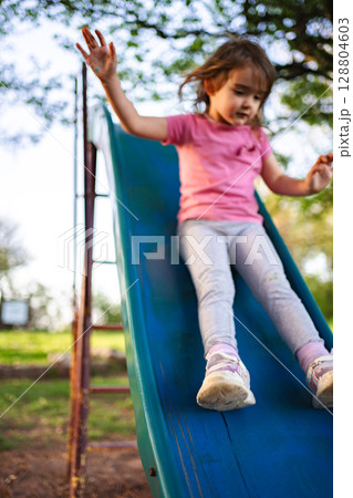 Young girl joyfully sliding down a playground slide in nature 128804603