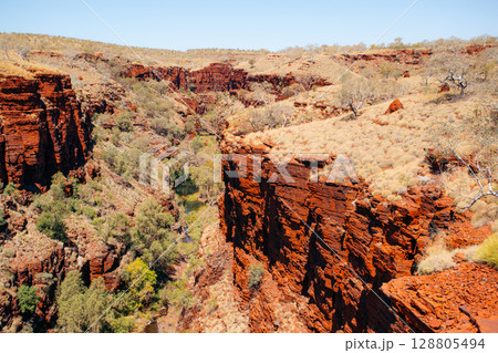 Red rock cliffs and sparse vegetation define Karijini National Park, Australia.. Red rock cliffs and sparse vegetation define Karijini National Park, Australia.. 128805494