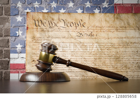 United States Constitution and American Flag On Wall with Gavel Resting on Table in Front. United States Constitution and American Flag On Wall with Gavel Resting on Table in Front. 128805658