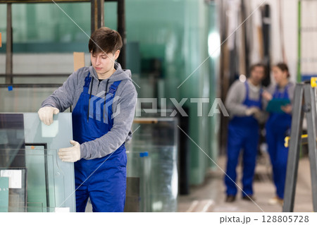 Young guy stacking glass sheets in factory Young guy stacking glass sheets in factory 128805728