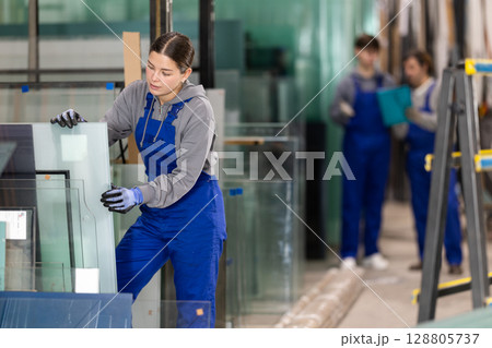 Girl glazer employee in blue overall works in glass processing shop Girl glazer employee in blue overall works in glass processing shop 128805737