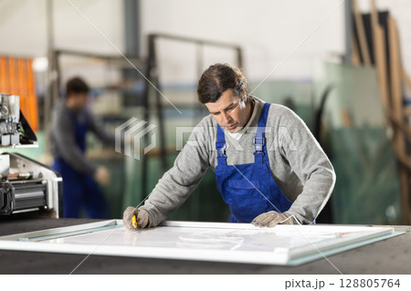 Adult man cutting sheet of glass in factory 128805764