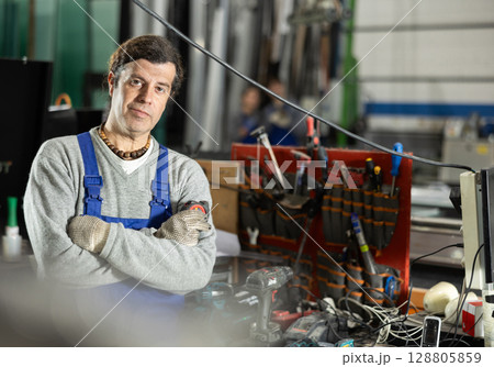 Man glazer employee in blue overall works in glass processing shop Man glazer employee in blue overall works in glass processing shop 128805859