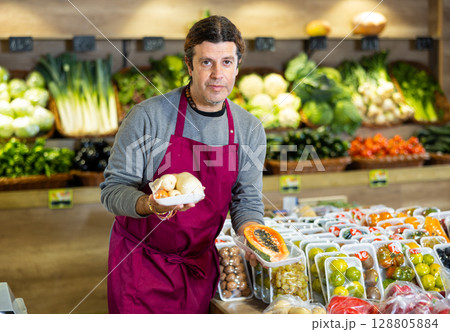 Male grocery store worker offers various packaged ripe fruits and vegetables Male grocery store worker offers various packaged ripe fruits and vegetables 128805884