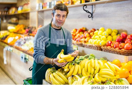 Positive male seller with ripe bananas on supermarket 128805894