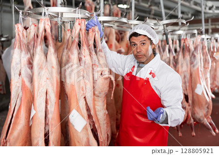 Male slaughterhouse worker showing mutton carcass in meat storage 128805921