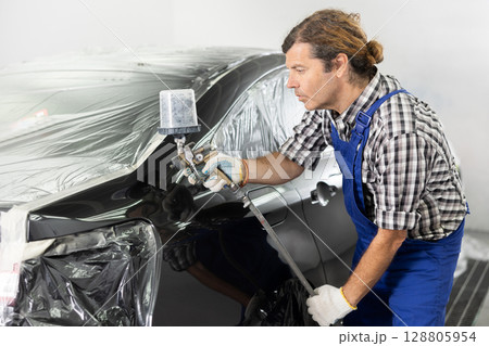 Repairman painter hand in protective glove with airbrush pulverizer painting car body 128805954