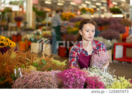 Positive female seller in apron holds dry flowers in hands Positive female seller in apron holds dry flowers in hands 128805973