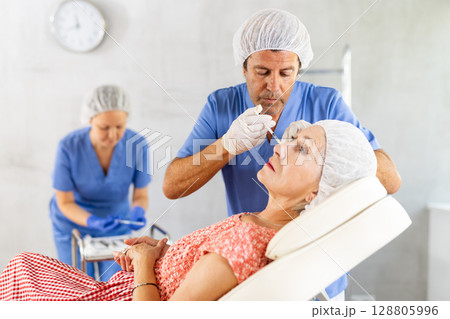 Elderly woman getting injections of hyaluronic acid in cheeks Elderly woman getting injections of hyaluronic acid in cheeks 128805996