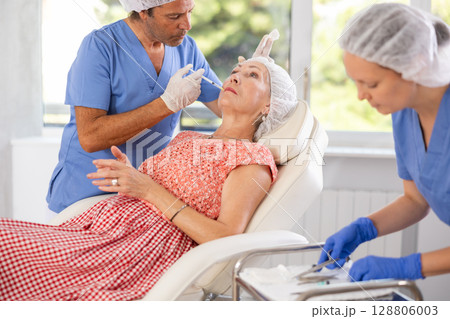 Woman applying rejuvenating treatments by male doctor. Woman applying rejuvenating treatments by male doctor. 128806003