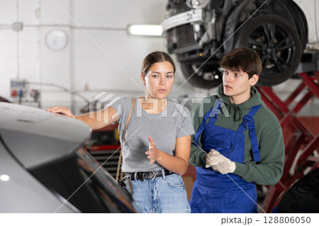 Girl who owns car talks about problems to an auto mechanic at car service center 128806050