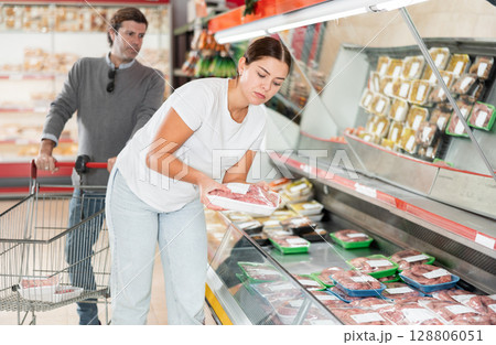 Man and woman looking for packaged raw sausages in grocery store 128806051