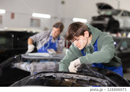 Young auto body technician repairing car bumper in workshop Young auto body technician repairing car bumper in workshop 128806071