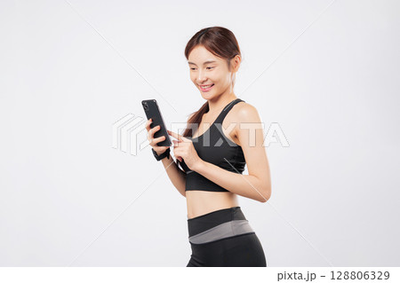 Holding phone and tapping phone screen, this sporty woman smiles in gym gear, embracing fitness, mobile apps, and a social lifestyle in one sleek look. isolated studio white background 128806329