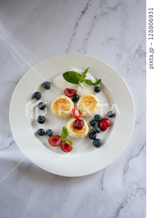 Cheesecakes with poppy seeds, blueberries, cherries and sour cream on white plate on marble table Cheesecakes with poppy seeds, blueberries, cherries and sour cream on white plate on marble table 128806931