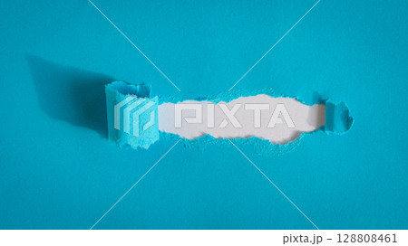 Hole ripped in blue paper on white background. 128808461