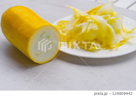 Sliced yellow zucchini on white plate on wood background. 128809442
