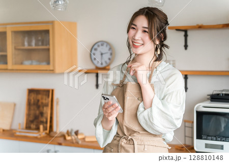 家のキッチン・ダイニングでスマホのアプリを使うアジア人女性 128810148