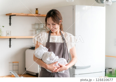 キッチンで赤ちゃんを抱っこする若いアジア人女性 128810677