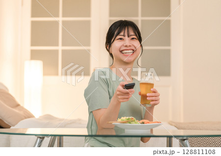 夕食に晩酌しながらテレビを見ながら笑う若いアジア人女性 128811108
