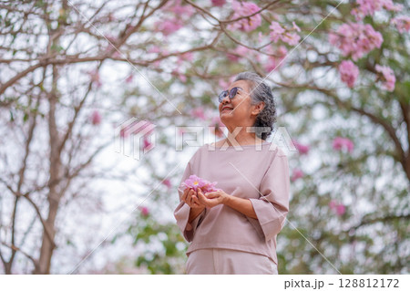 Elderly women with gray hair enjoying a beautiful moment together outdoors, surrounded by blooming pink flowers expressions reflect deep friendship and happiness relaxation with nature. 128812172