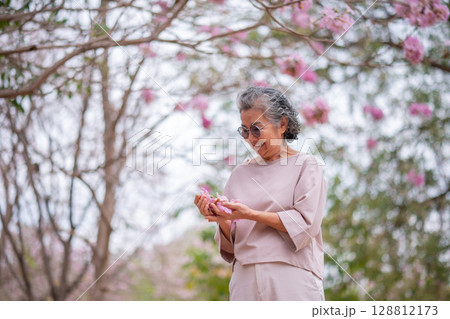 Elderly women with gray hair enjoying a beautiful moment together outdoors, surrounded by blooming pink flowers expressions reflect deep friendship and happiness relaxation with nature. 128812173