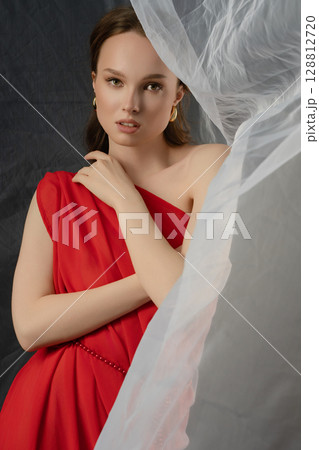 Woman poses in elegant red gown against dramatic studio backdrop, conveying a range of emotions and expressions 128812720
