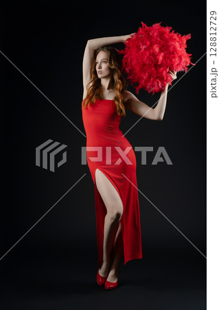 Emotional woman posing gracefully in a luxurious red dress with feathers in a studio setting Emotional woman posing gracefully in a luxurious red dress with feathers in a studio setting 128812729
