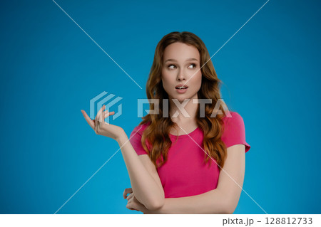 Woman poses in a studio with a vibrant blue background, expressing confidence and charm through her playful gesture and expression 128812733