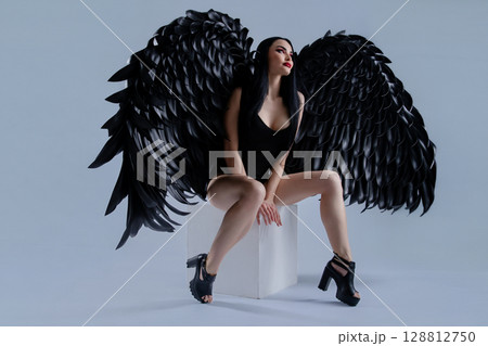 Woman in black lingerie with striking wings poses elegantly in a studio setting Woman in black lingerie with striking wings poses elegantly in a studio setting 128812750