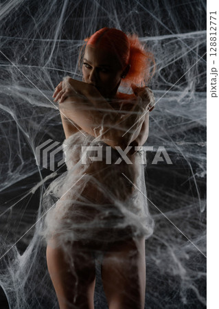 Red-haired woman caught in a delicate web trap, showcasing beauty and intrigue 128812771