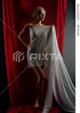 Elegant woman posing with sheer fabric in a studio setting 128812784